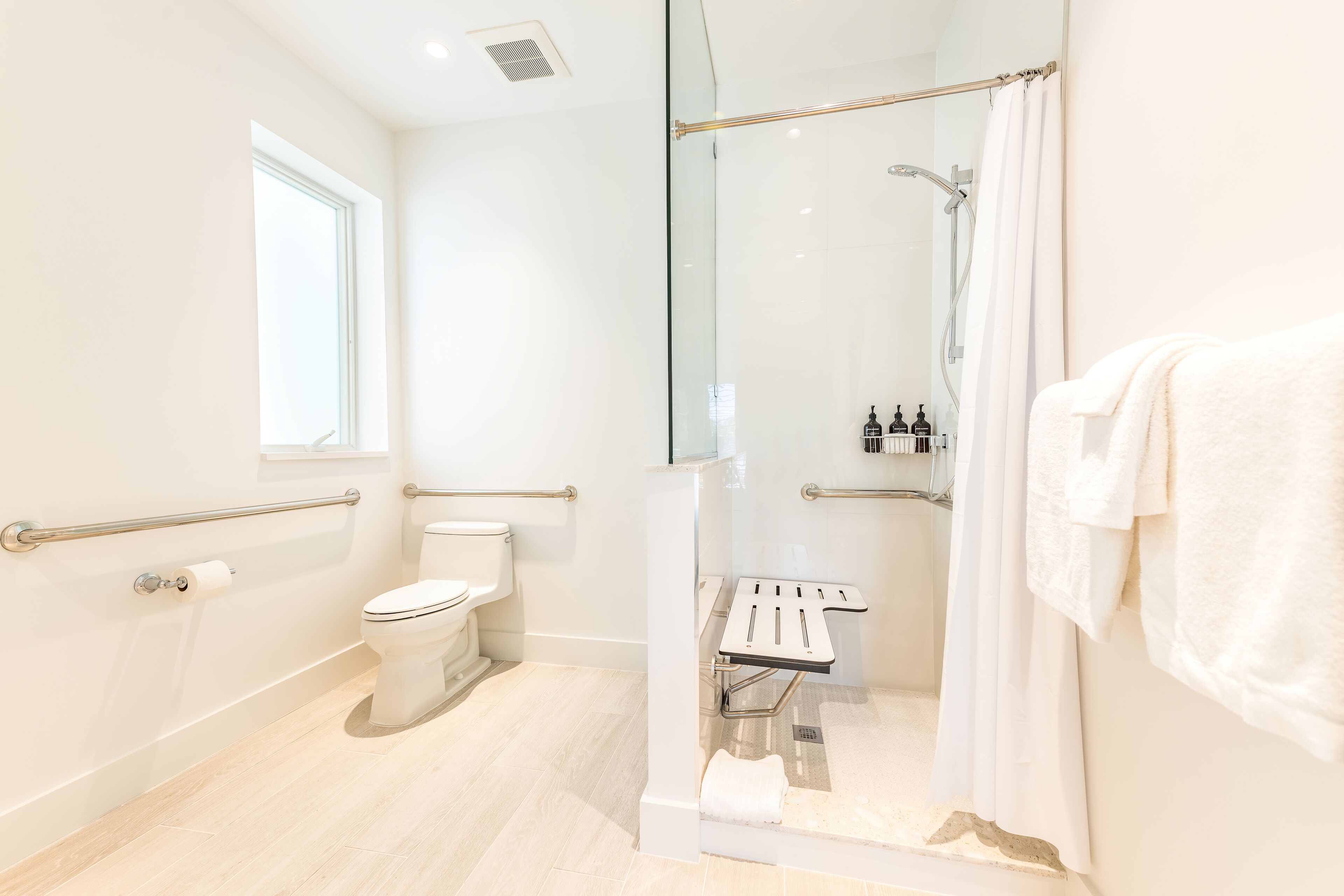 A modern bathroom with a glass-enclosed shower, a toilet, and a bench.