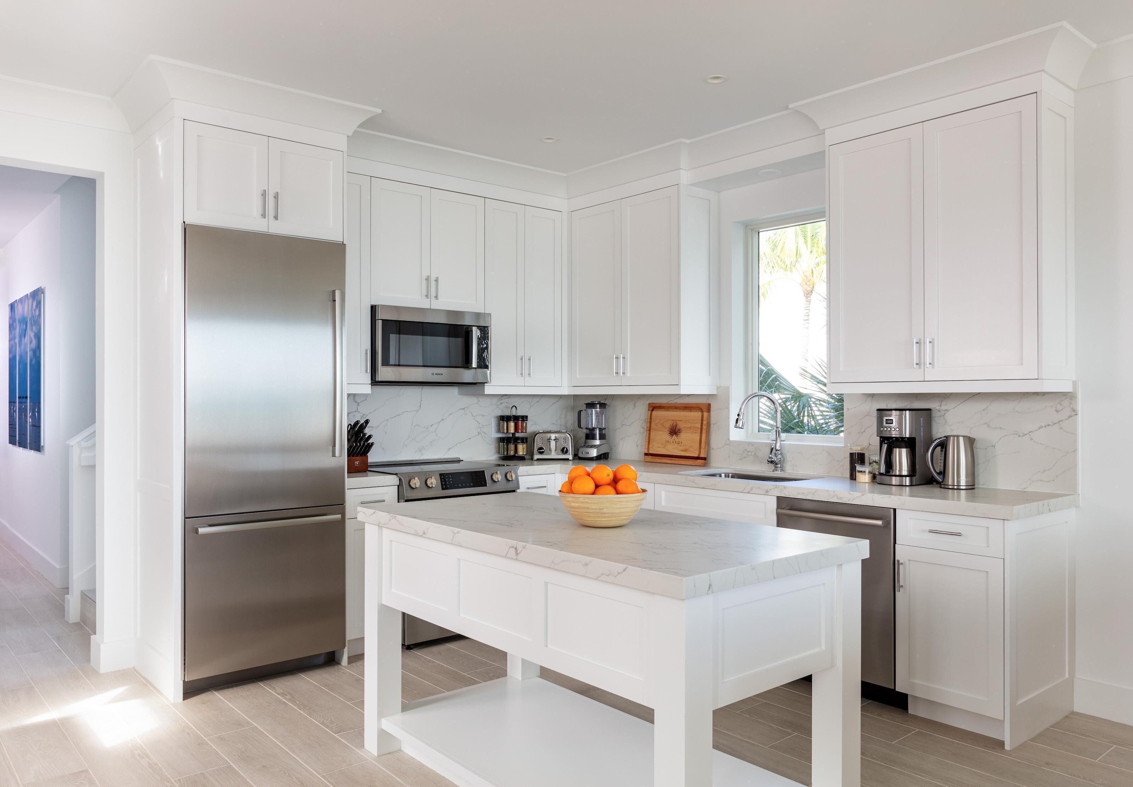 A modern kitchen with white cabinetry, stainless steel appliances, and a marble countertop.