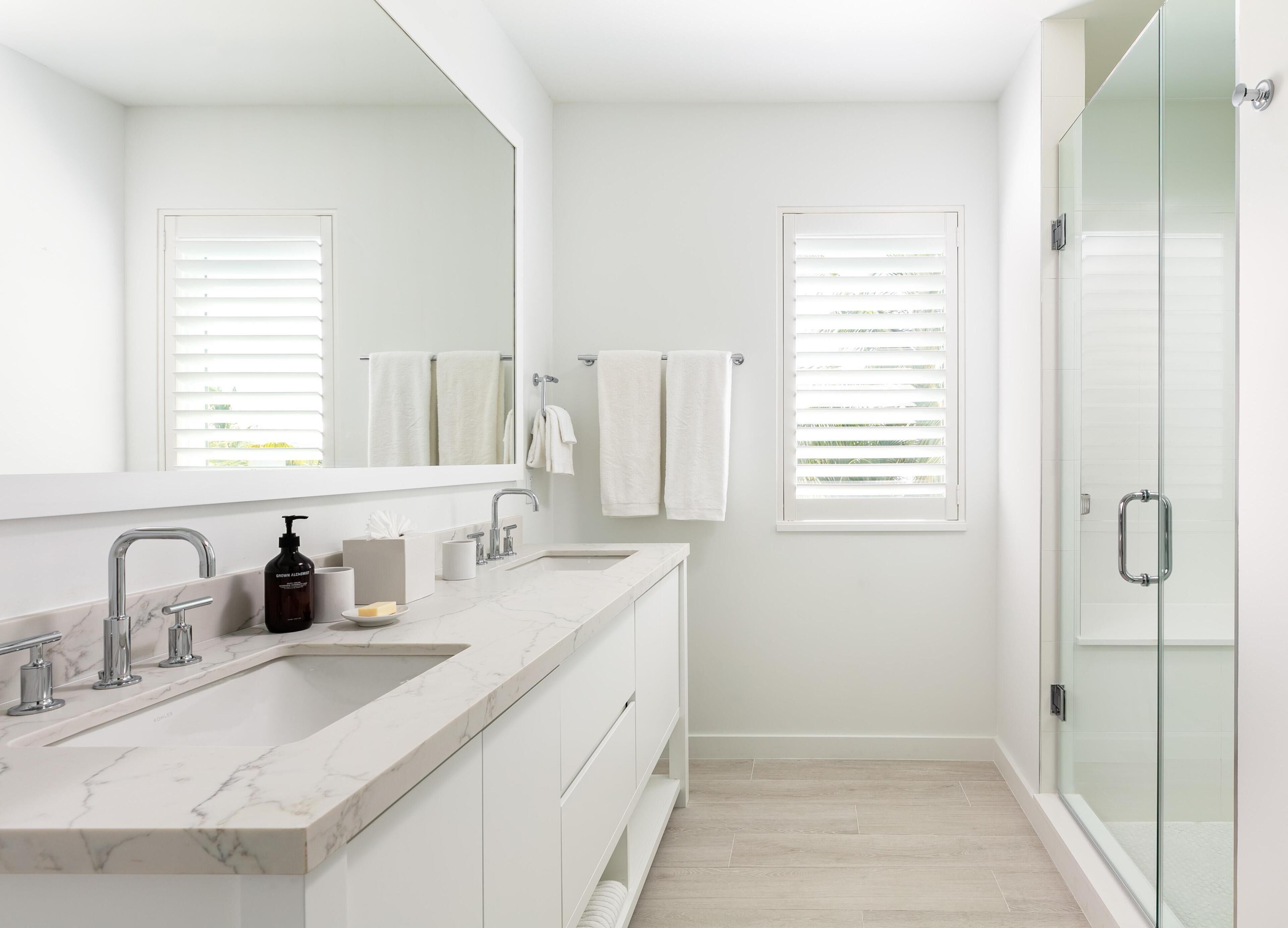 A modern bathroom with a marble sink, a glass shower enclosure, and white towels.