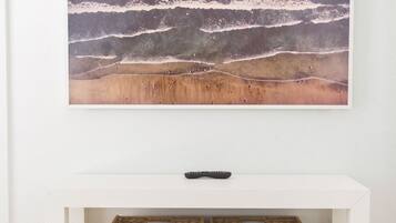 A white console table with a framed artwork above and two wicker baskets below.
