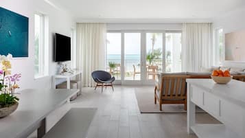 A modern hotel room with a balcony, a flat-screen TV, a dining area, and a seating space.