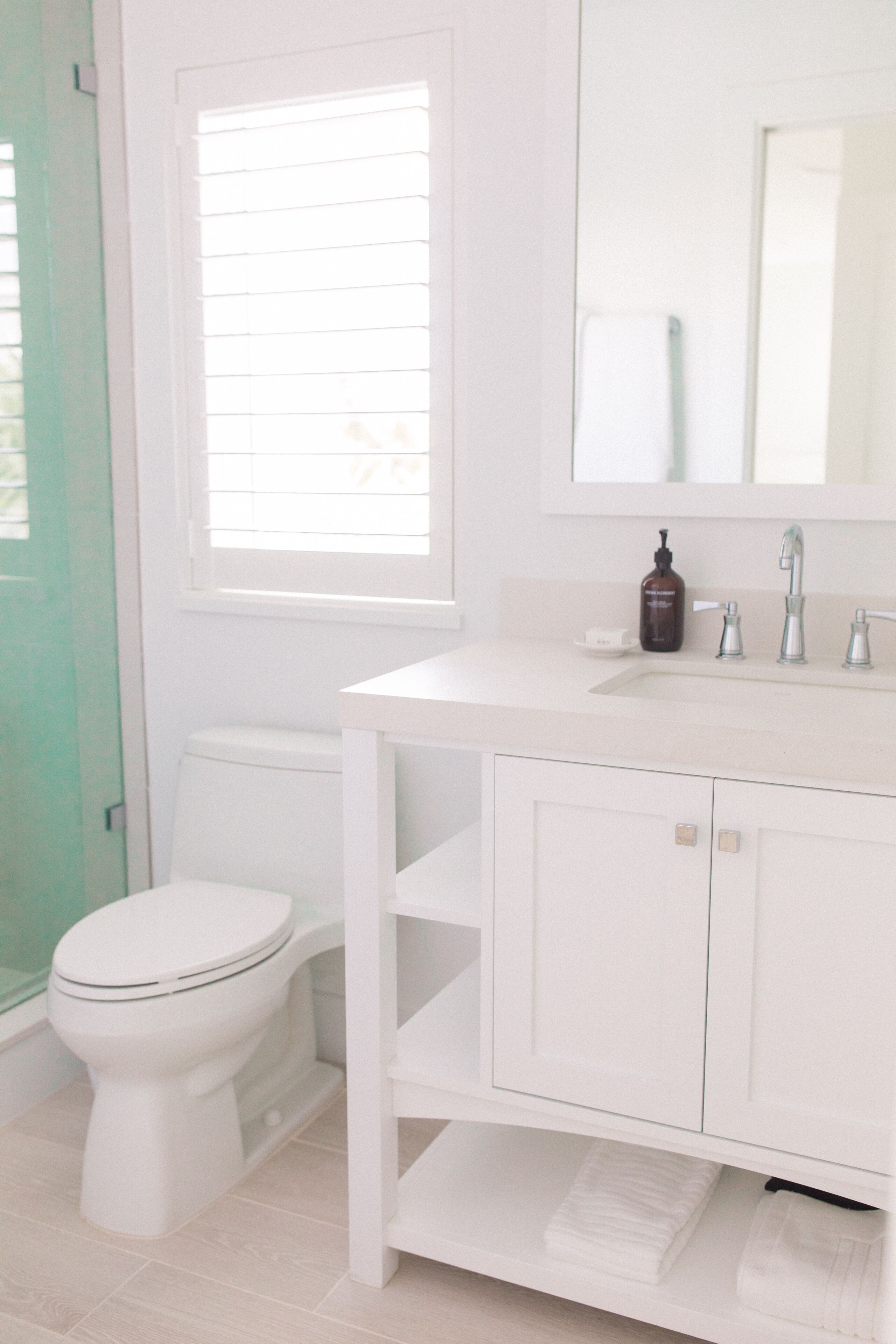 Une salle de bain blanche avec des toilettes, un lavabo avec un miroir et une fenêtre.