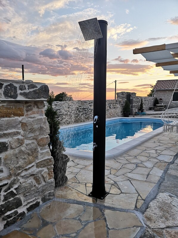 Relax in a refreshing outdoor shower, adjacent to a swimming pool and surrounded by a patio area.