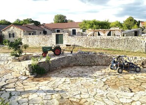 Surrounded by stone walls, this charming courtyard features a green tractor and off-road vehicle, amidst lush trees and shrubs.