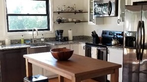 A modern kitchen with a wooden island, black bar stools, stainless steel appliances, and pendant lighting. - Rappahannock River Unplugged (Jamaica)