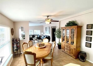 A dining area with a wooden table, chairs, a ceiling fan, a cabinet, and a potted plant. - J and M Retreat - New in ground heated pool 💦 (Mattawa)
