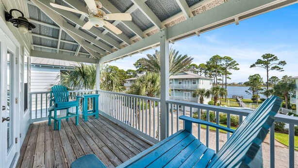 A covered porch with wooden flooring, turquoise chairs, and a ceiling fan.