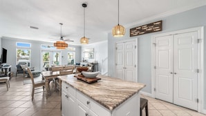 A spacious kitchen with a marble countertop, white cabinetry, and pendant lights.