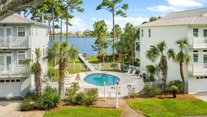 A residential property with a swimming pool, surrounded by a white fence, palm trees, and a view of a lake.