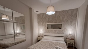 Ein modernes Schlafzimmer mit einem großen Spiegel, einem Bett mit gemustertem Bettbezug, Nachttischlampen und einer Hängeleuchte.