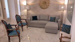 Ein Wohnzimmer mit grauem Ecksofa, zwei blauen Sesseln, einem Holzsessel und einer Wanddekoration.