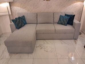 A grey sectional sofa with blue patterned cushions, positioned on a marble floor with a leaf-patterned wallpaper backdrop. - New apartment near the Duomo with Wi-Fi and an elevator (Firenze)