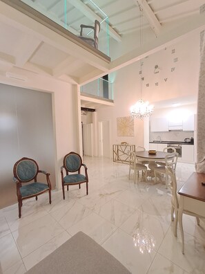 A spacious living area with a high ceiling, a dining set, and a kitchen in the background.