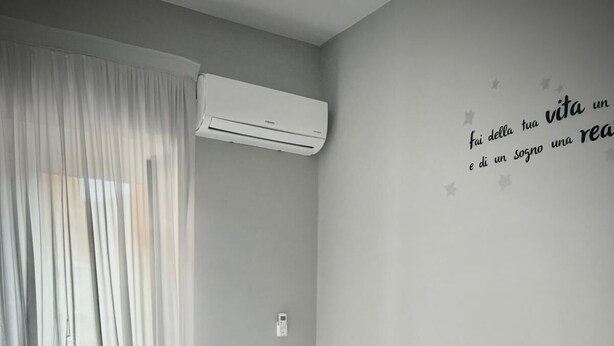 A modern bedroom with a bed, pillows, a bedside lamp, and a wall-mounted air conditioner. - B&B Rianna House (Naples)