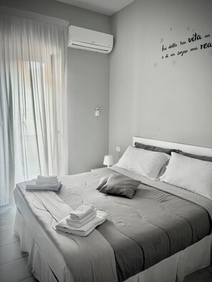 A modern bedroom with a bed, pillows, a bedside lamp, and a wall-mounted air conditioner. - B&B Rianna House (Naples)