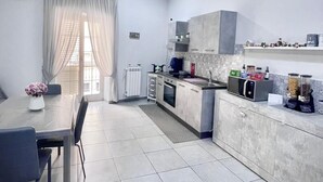A modern kitchen with grey cabinets, a dining table with chairs, and a window with sheer curtains. - B&B Rianna House (Naples)