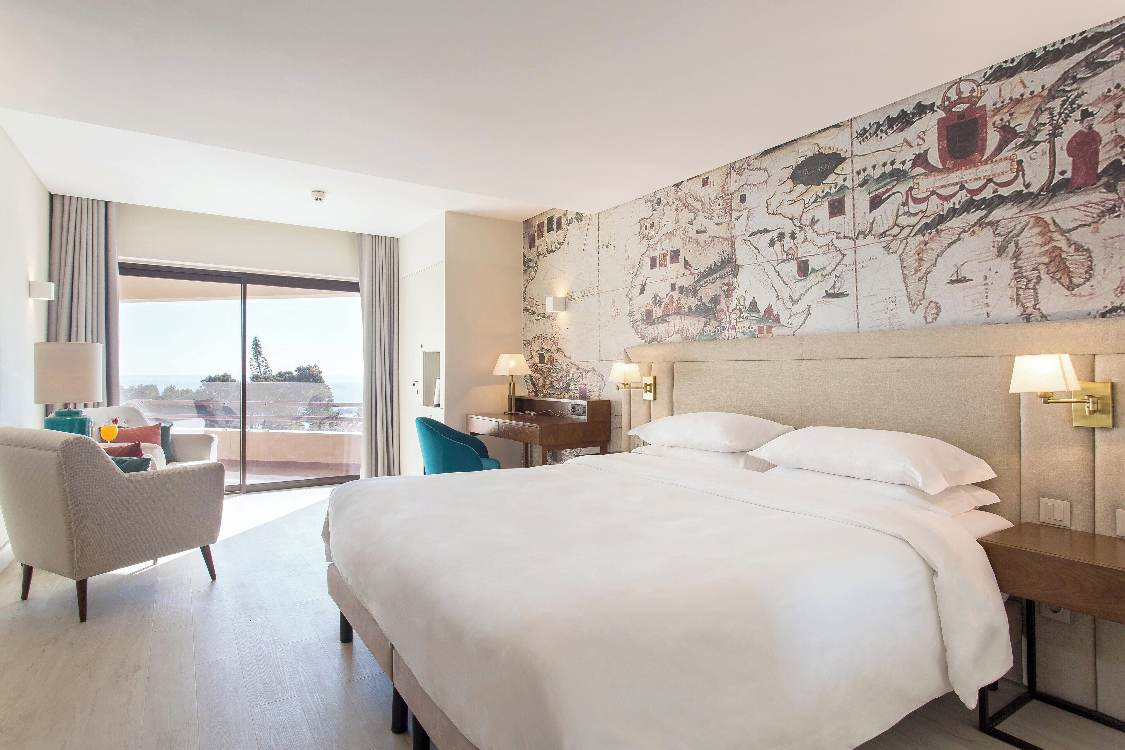 A hotel room with a large bed, a desk, a chair, and a large window with a view.