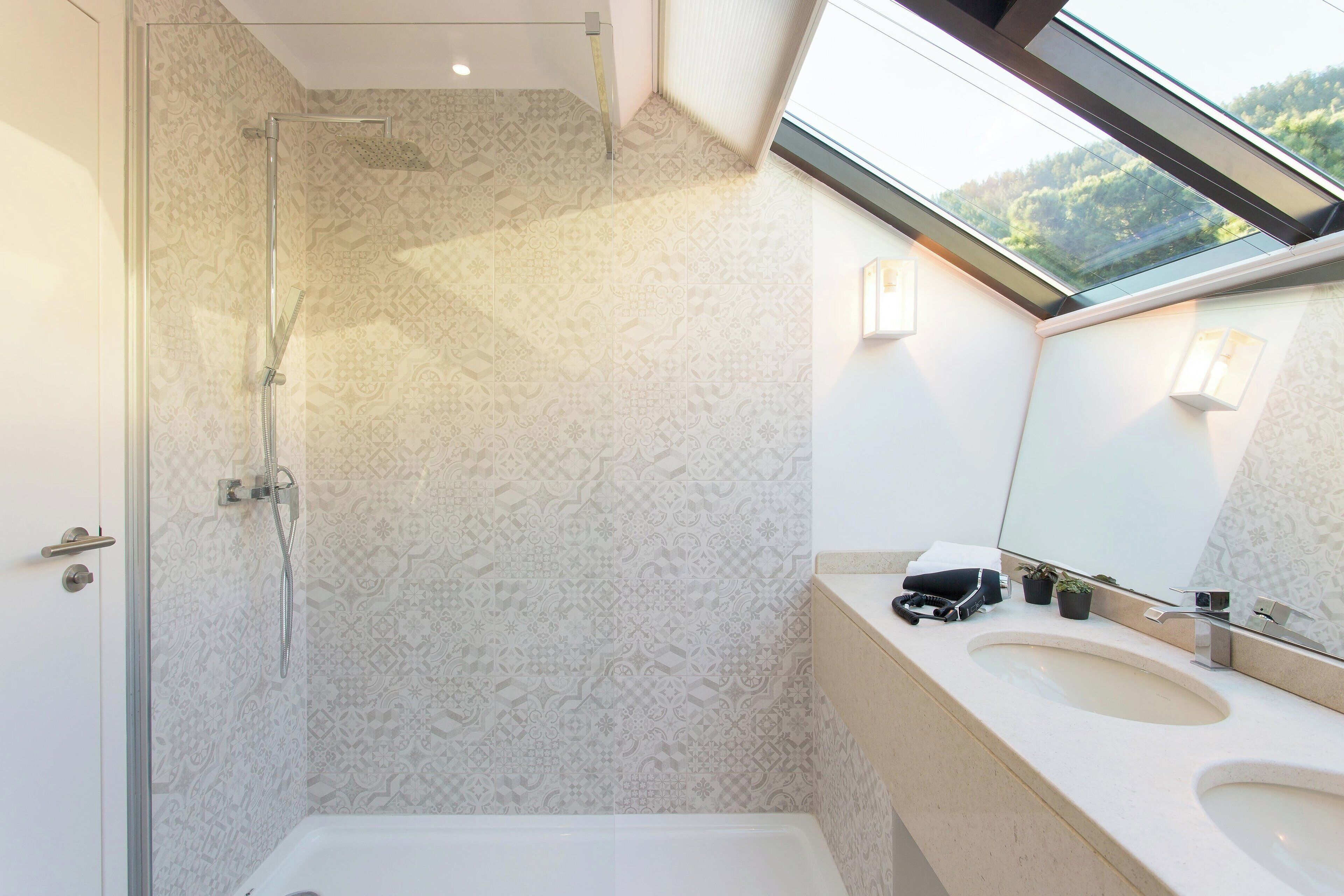 Un baño con papel tapiz estampado, ducha con cerramiento de vidrio, un espejo grande y un lavabo con encimera.
