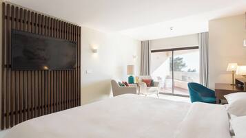 Ein Hotelzimmer mit einem großen Bett, einem flachbildfernseher an einer Holzvertäfelung, einer Sitzecke mit Stühlen und einem Balkon mit Aussicht.
