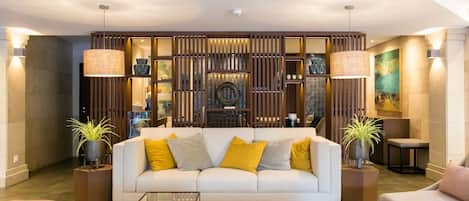 A modern living room with a white sofa, yellow and grey cushions, two side tables with potted plants, and a glass coffee table.