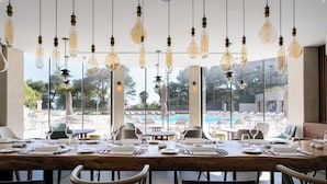 Un comedor con vista a la piscina, con una mesa larga dispuesta para una comida, lámparas colgantes y una decoración interior moderna.