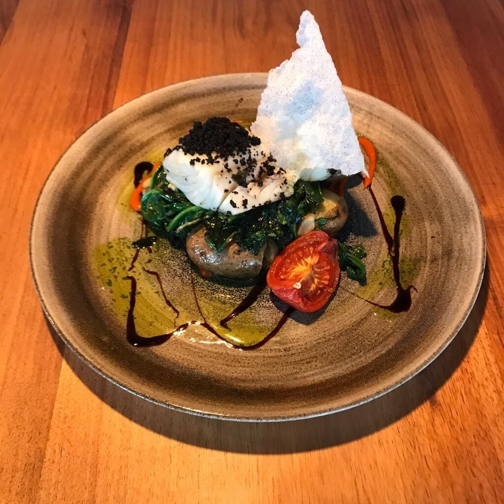 A plate of food with a poached egg, mushrooms, spinach, and a cherry tomato, served on a ceramic plate.