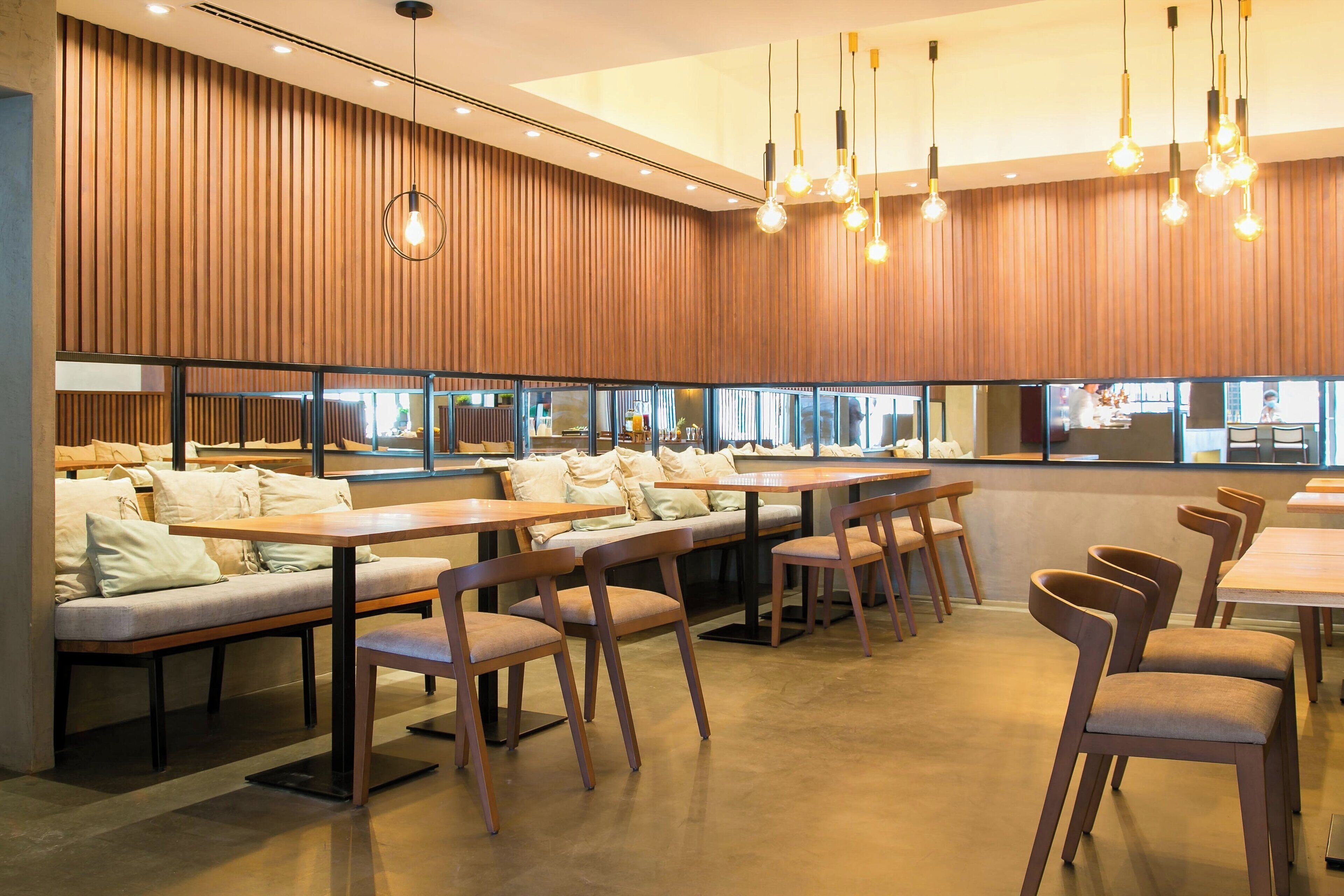 Un restaurante moderno con paneles de madera, mesas largas comunitarias y zonas de estar con cojines.