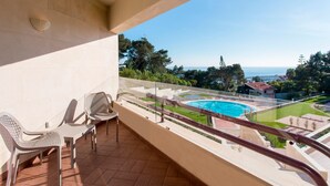 Un balcon avec deux chaises, une vue sur une piscine et un ciel dégagé.