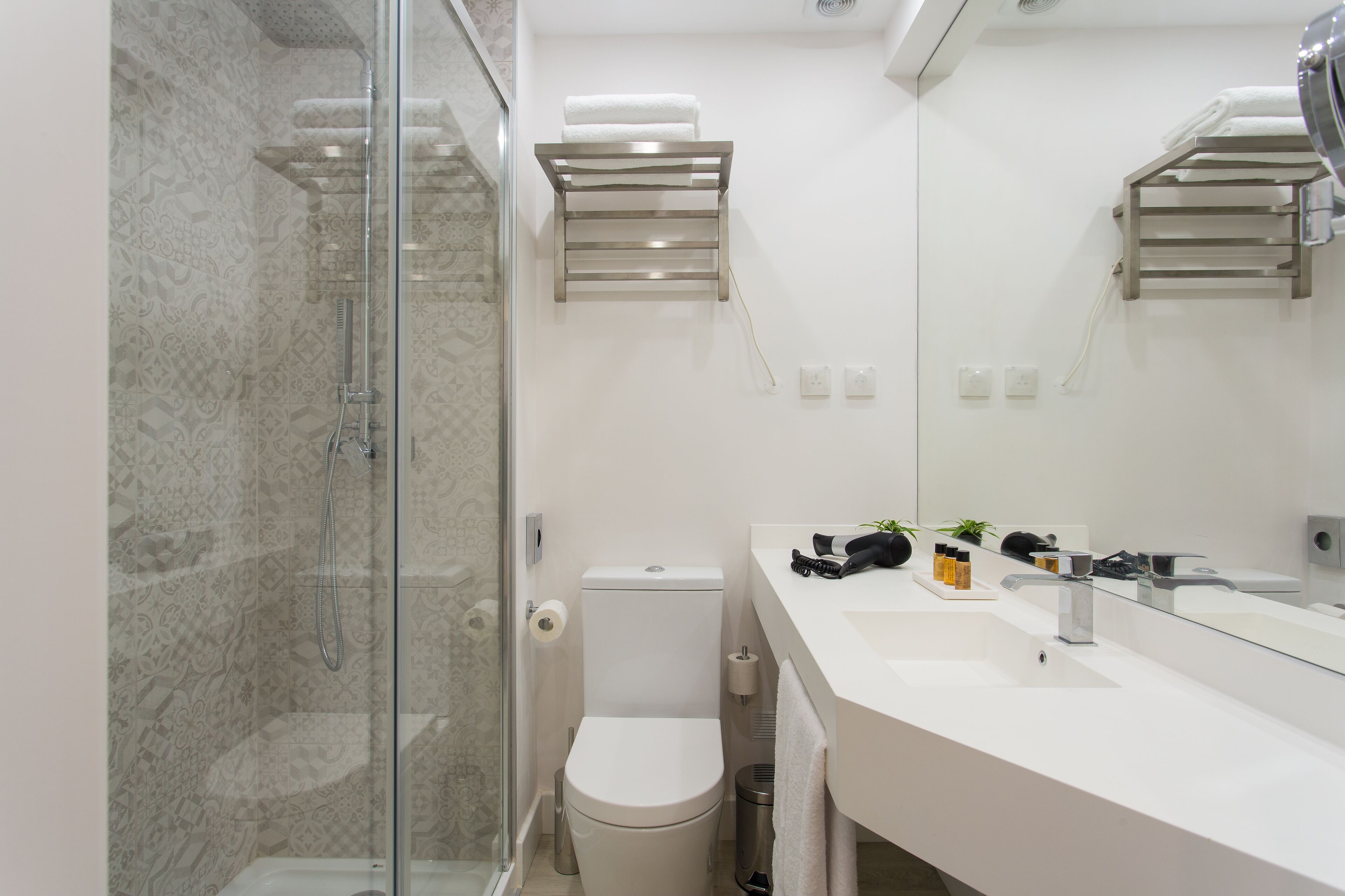 A modern bathroom with a glass shower enclosure, a toilet, a sink with a mirror, and towel racks.