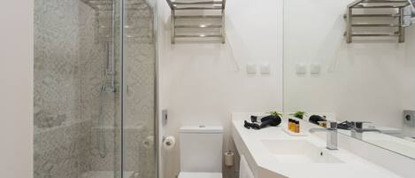 A modern bathroom with a glass shower enclosure, a toilet, a sink with a mirror, and towel racks.