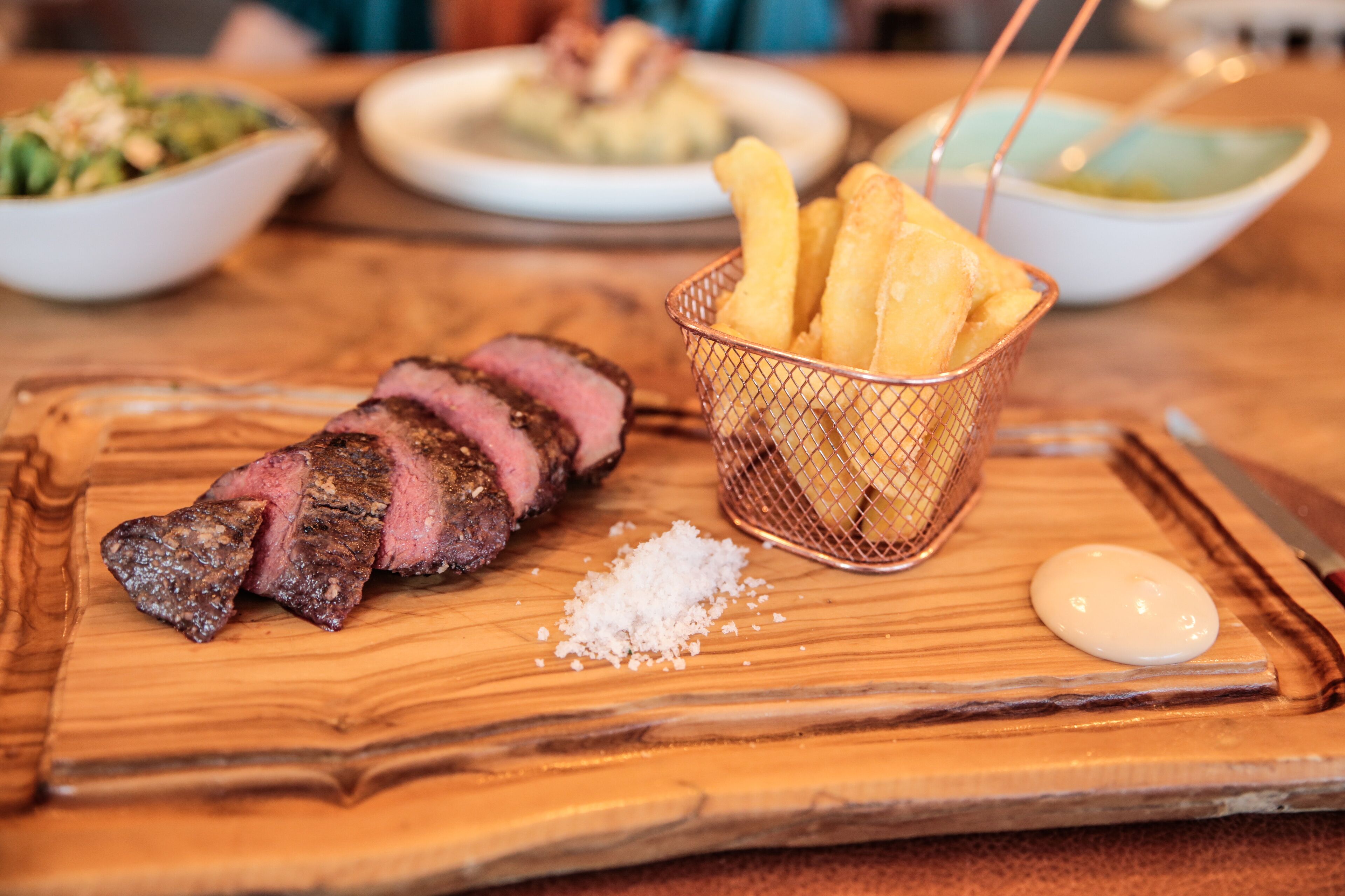 En træskærebræt med bøf, pommes frites og tilbehør.