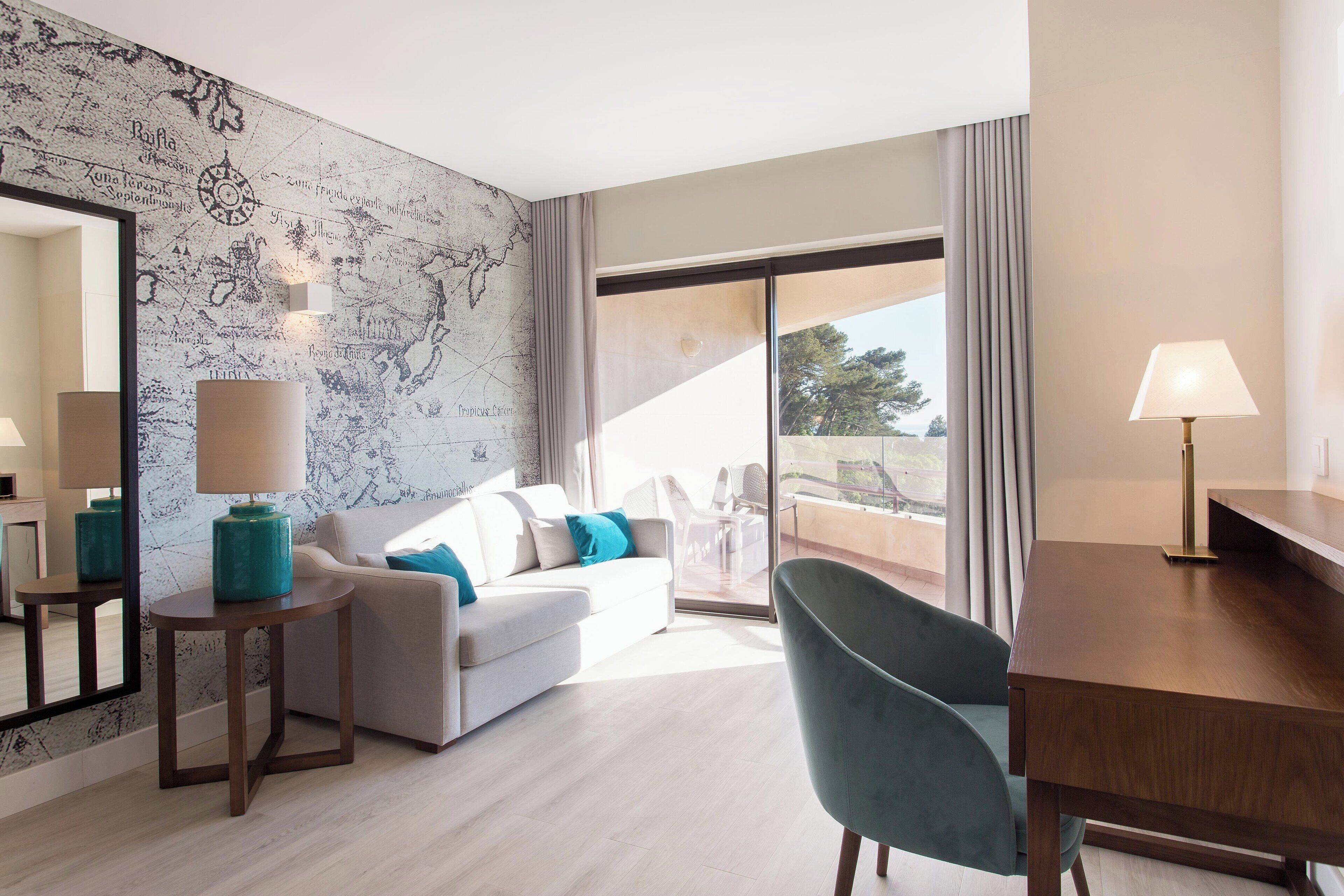 Una habitación de hotel moderna con un ventanal grande, un sofá, un escritorio y una silla.