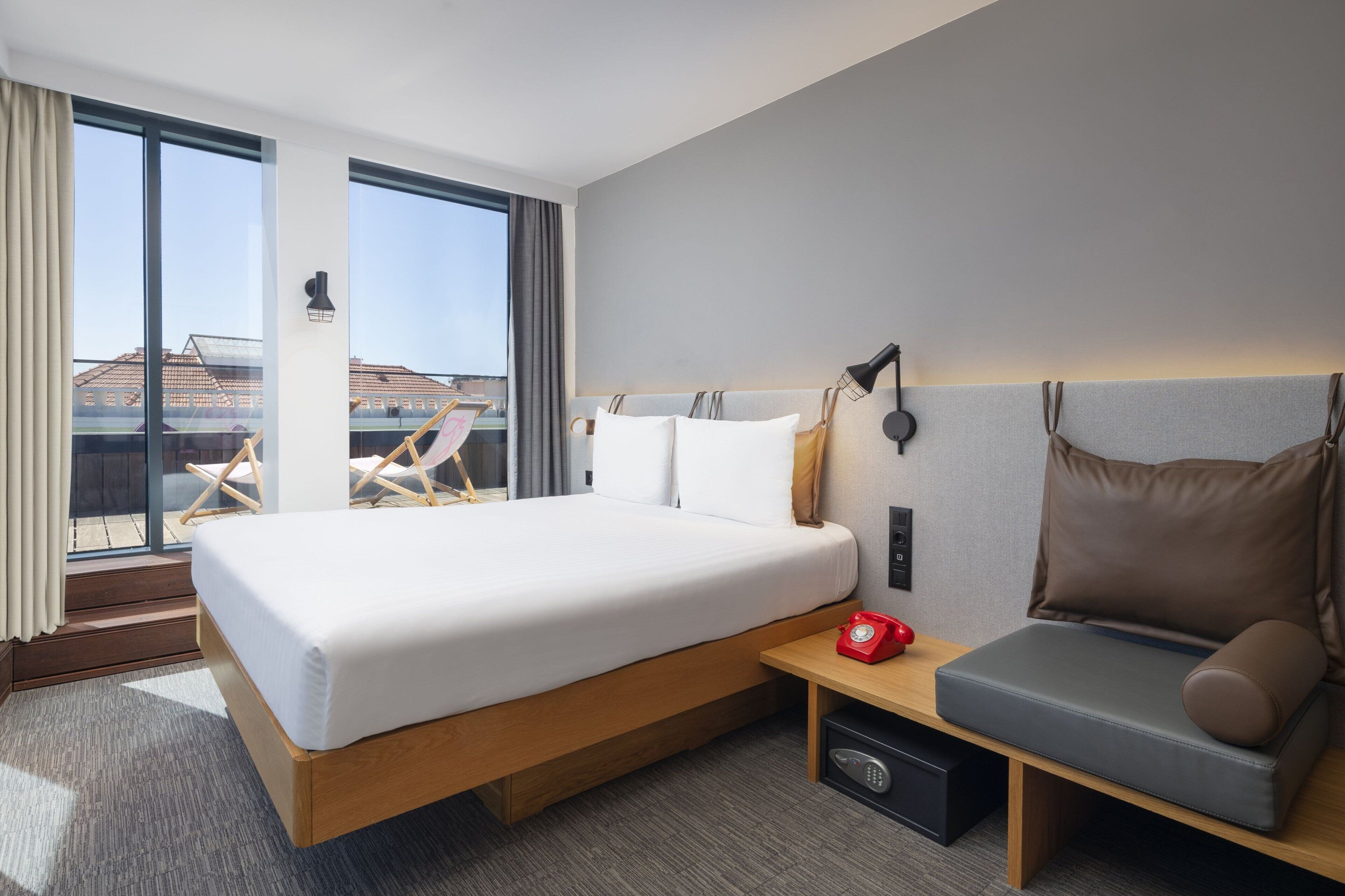 Et moderne hotelværelse med en stor seng, et sengebord med en rød telefon og et siddeområde med en polstret bænk.