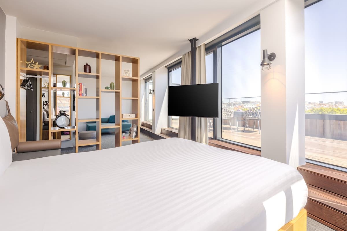 Een moderne hotelkamer met een groot bed, een houten garderobe, een flatscreen televisie en een balkon met uitzicht over de stad.
