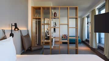 A hotel room with a bed, a wooden partition, a TV, and a view of the outside through large windows.