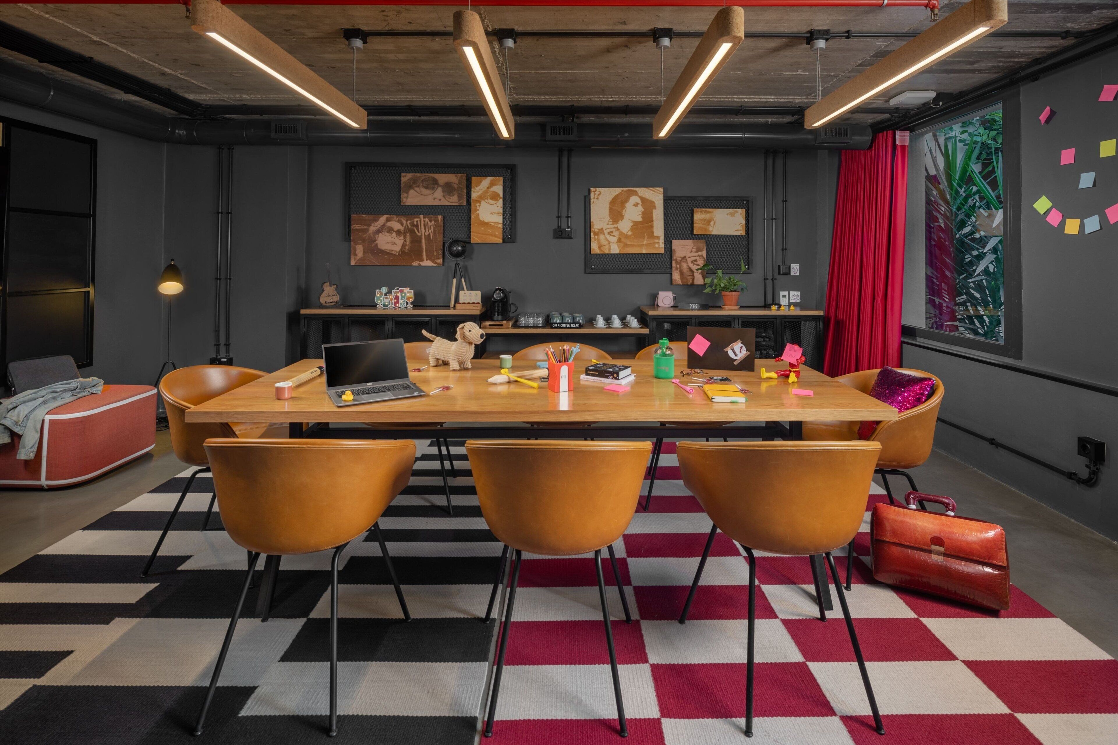 A modern meeting room with a long table, four chairs, and a laptop.