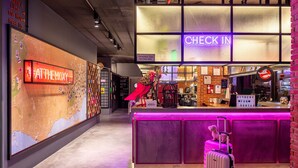 A hotel reception area with a large map on the wall, a neon 'CHECK IN' sign, and a counter with a 'HITHERE' sign. - Moxy Lisbon City (Lisbon)