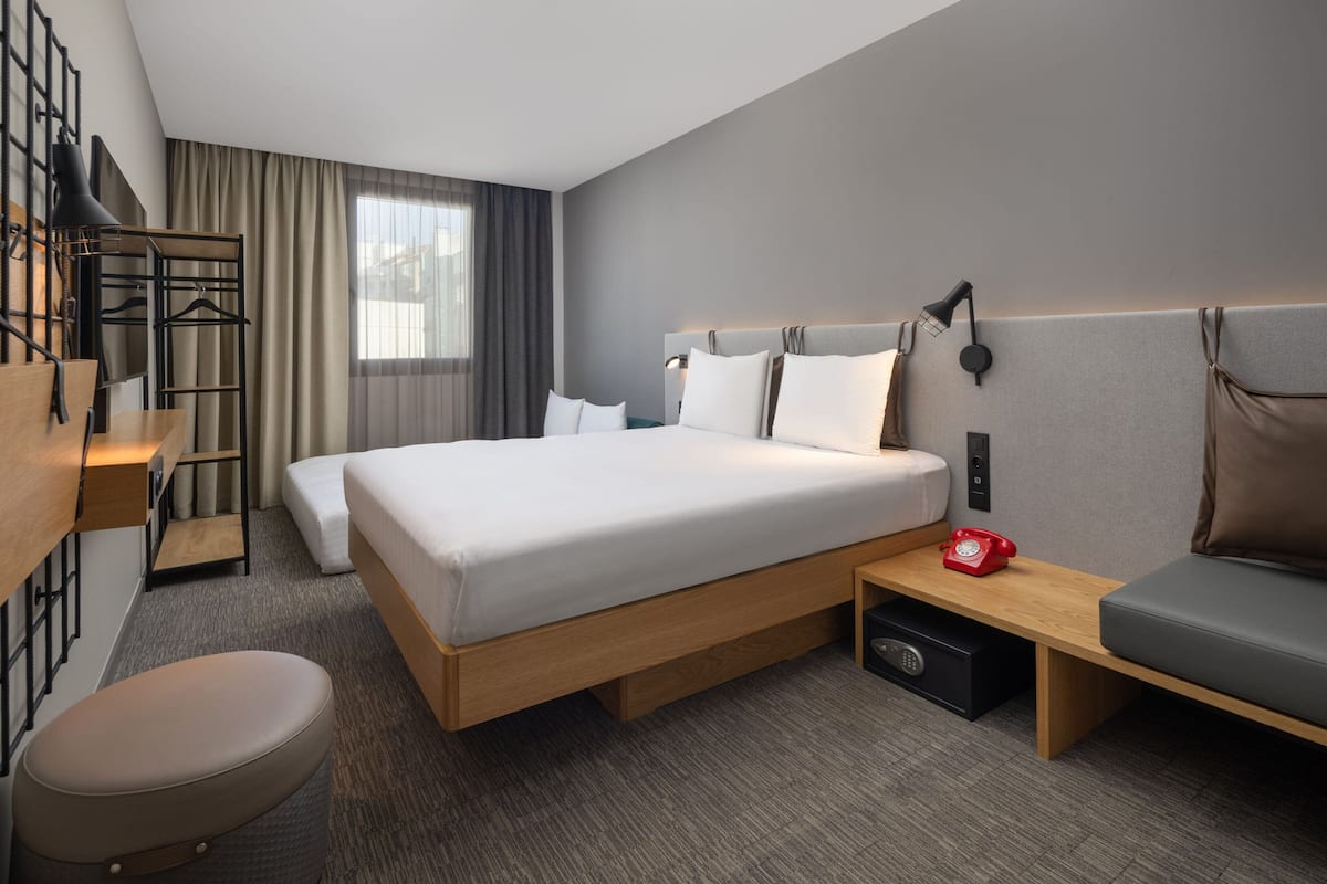 Een moderne hotelkamer met een groot bed, een nachtkastje met rode telefoon, een zithoekje en een bureau met stoel.