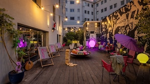 An outdoor patio area with string lights, wooden chairs, a table with a neon sign, and a mural on the wall. - Moxy Lisbon City (Lisbon)