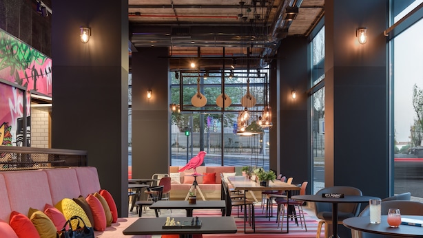 A modern cafe with a pink sofa, black tables, and a red bird decoration. - Moxy Lisbon City (Lisbon)