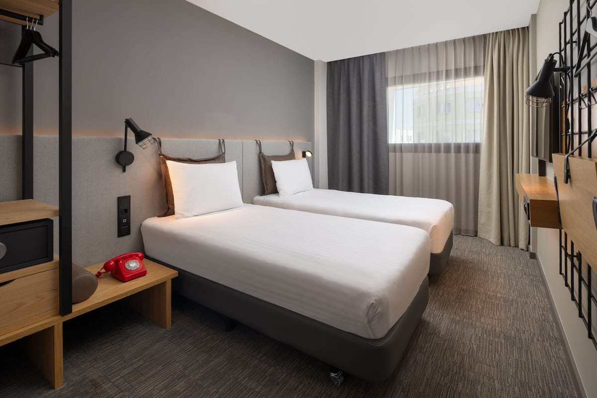 Een hotelkamer met twee bedden, een bureau met telefoon en een raam met gordijnen.