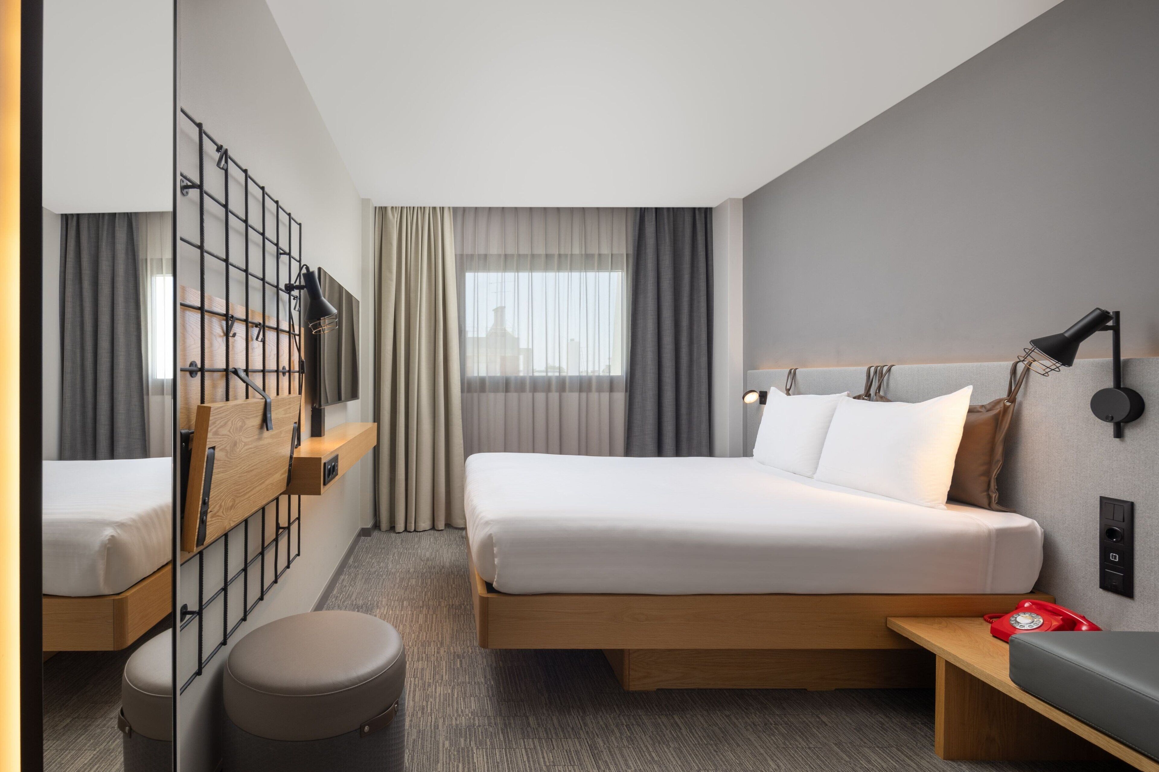 Una camera d'albergo moderna con un ampio letto, una scrivania, una sedia, un tavolino, una lampada e un telefono.