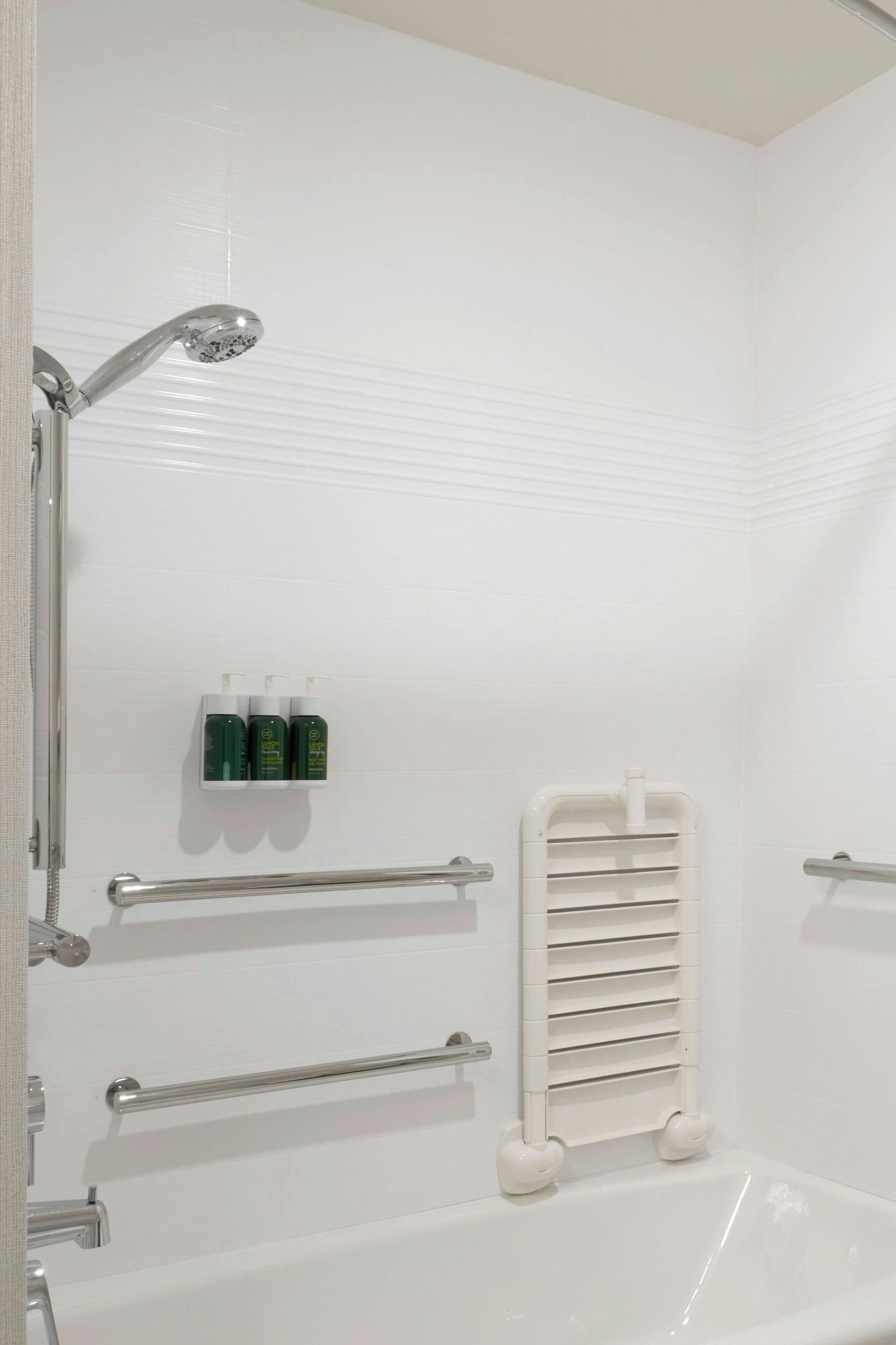 A modern bathroom with a white bathtub, grab bars, a handheld showerhead, and a towel rack.