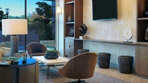Una sala de estar moderna con un televisor grande, asientos cómodos, una araña y vistas al exterior.