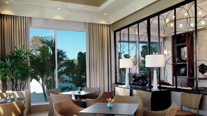 Una habitación de hotel moderna con un ventanal grande, muebles de mimbre y un espejo decorativo.