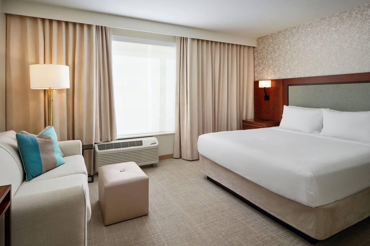 A hotel room with a large bed, a sofa, a lamp, and a window with curtains.