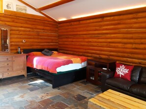 A log cabin room with a bed, dresser, and a leather couch. - Log cabin on the James River in Alberta (James River Bridge)