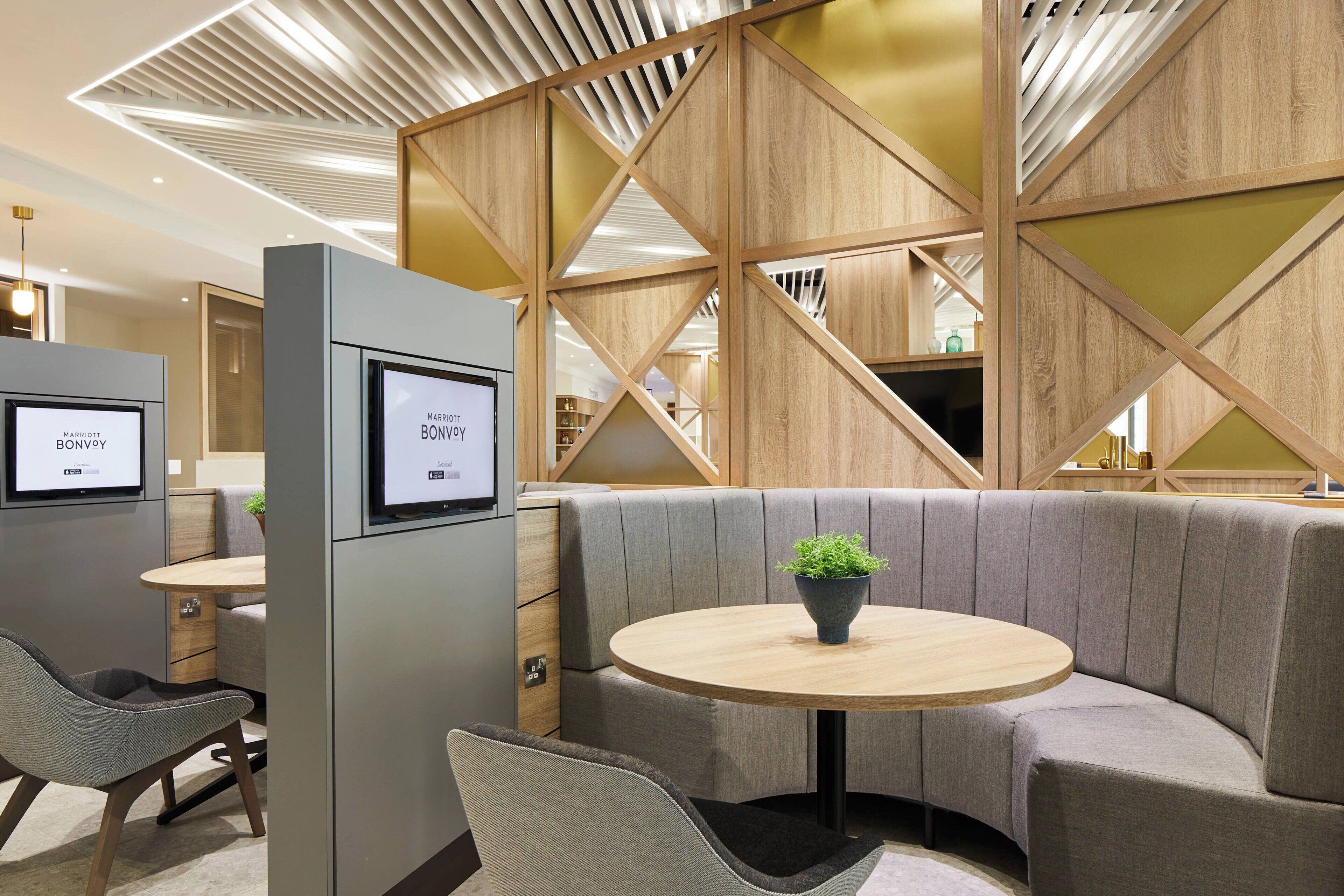 A modern hotel lobby with a seating area featuring a round wooden table and cushioned benches.