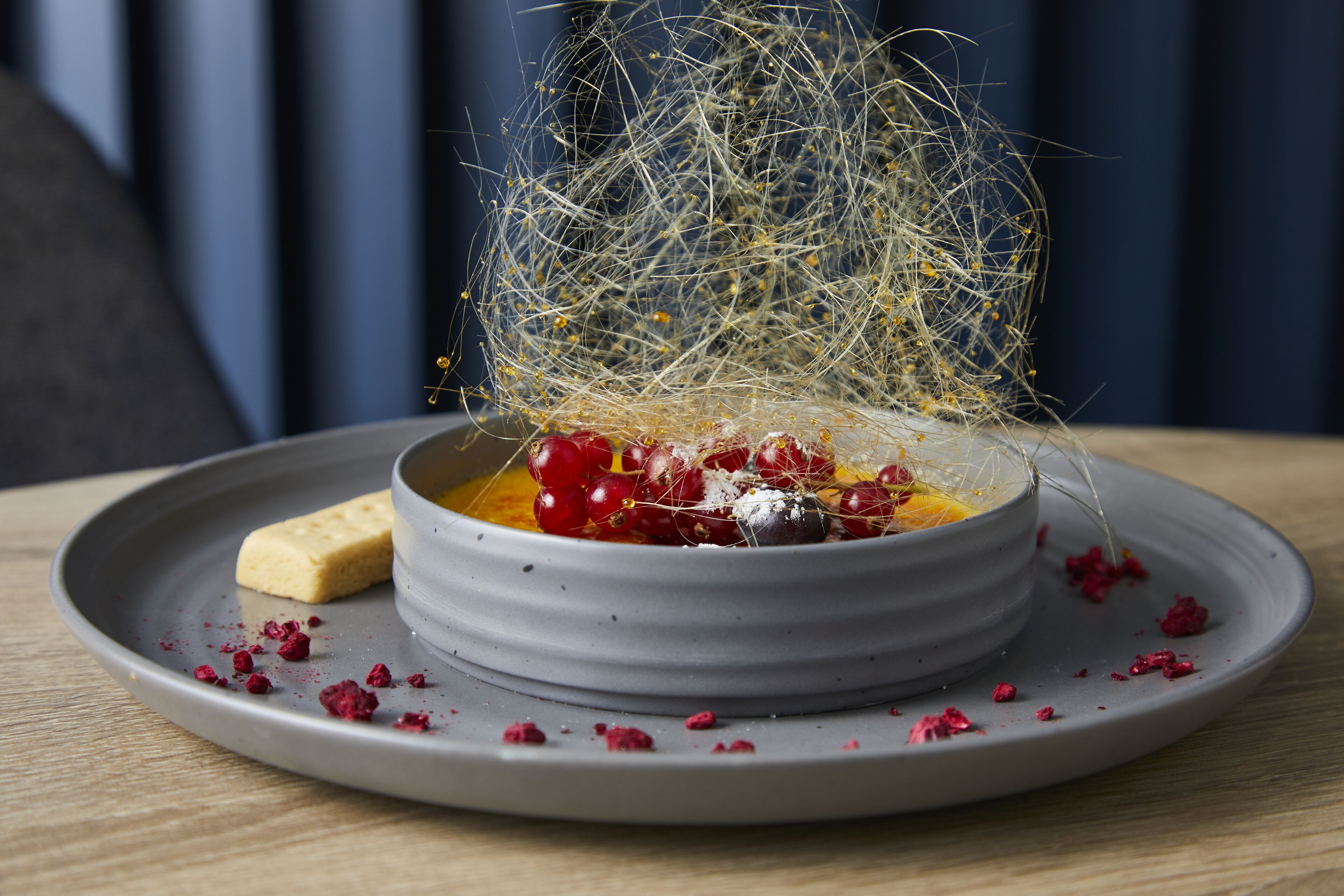 A dessert in a bowl on a plate, with a decorative spider web and berries.
