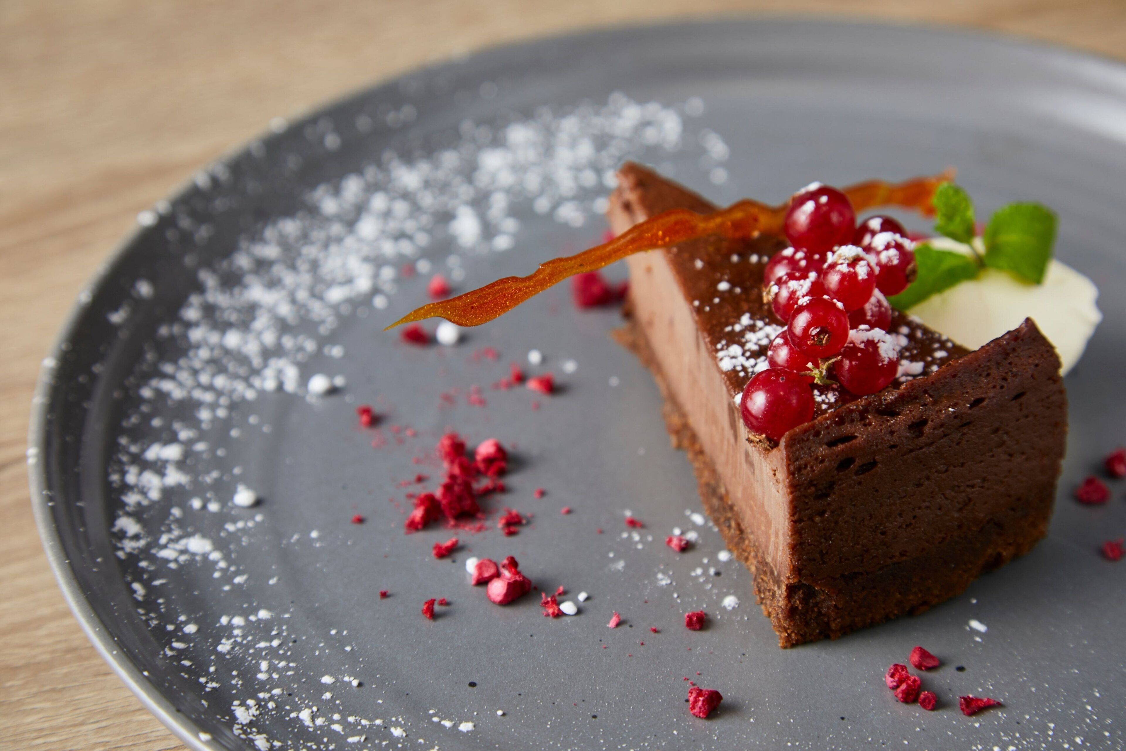 Una fetta di torta al cioccolato con frutti di bosco e foglie di menta su un piatto.